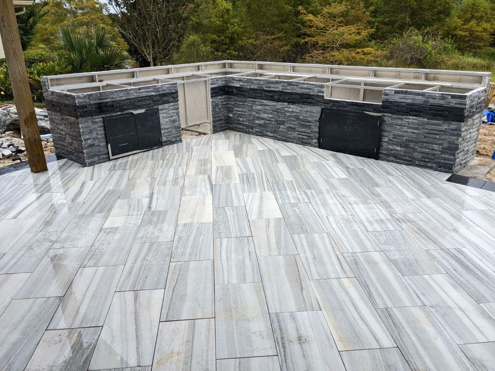 Modern outdoor kitchen with stone walls, concrete countertops, and tiled flooring.