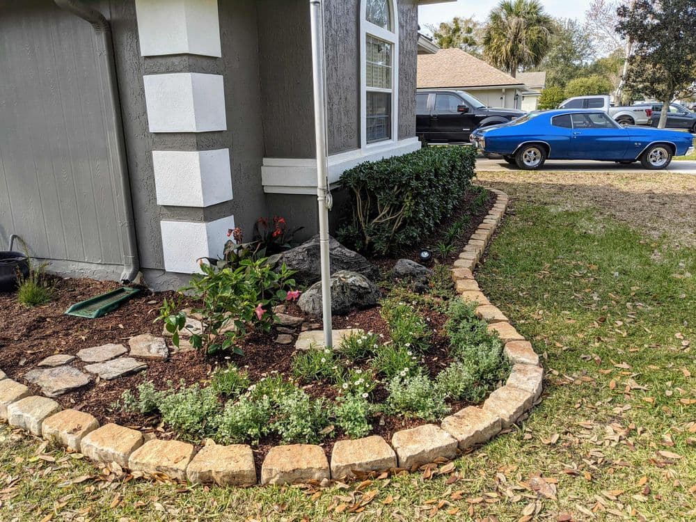 Landscaped yard with stone borders, colorful flowers, and a classic blue car parked nearby.