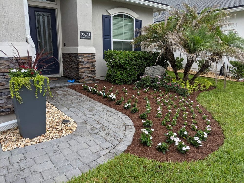 Front garden featuring vibrant flowers, palm trees, and stone landscaping at a home entrance.