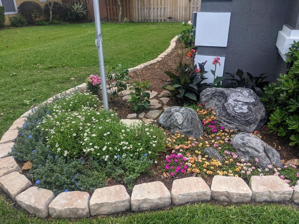 Colorful flowerbed with rocks and lush greenery beside a home.