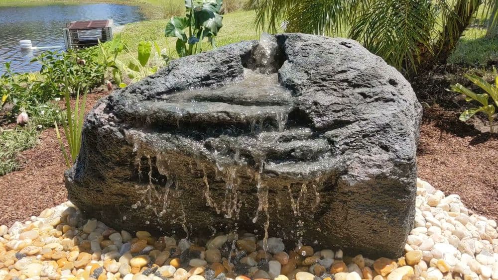 Rock waterfall feature with cascading water over stones in a landscaped garden.