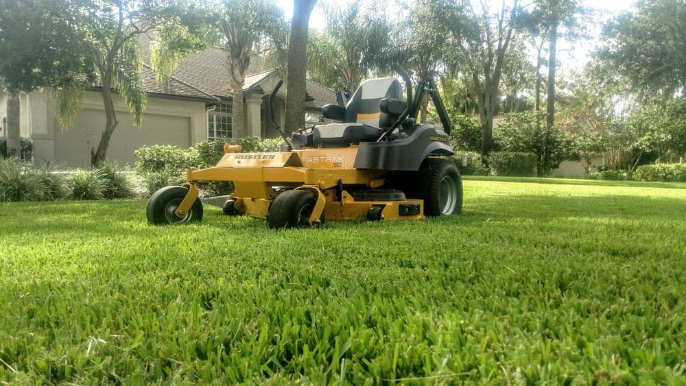 Hustler Fastrak zero-turn lawn mower on a lush green lawn in a residential area.